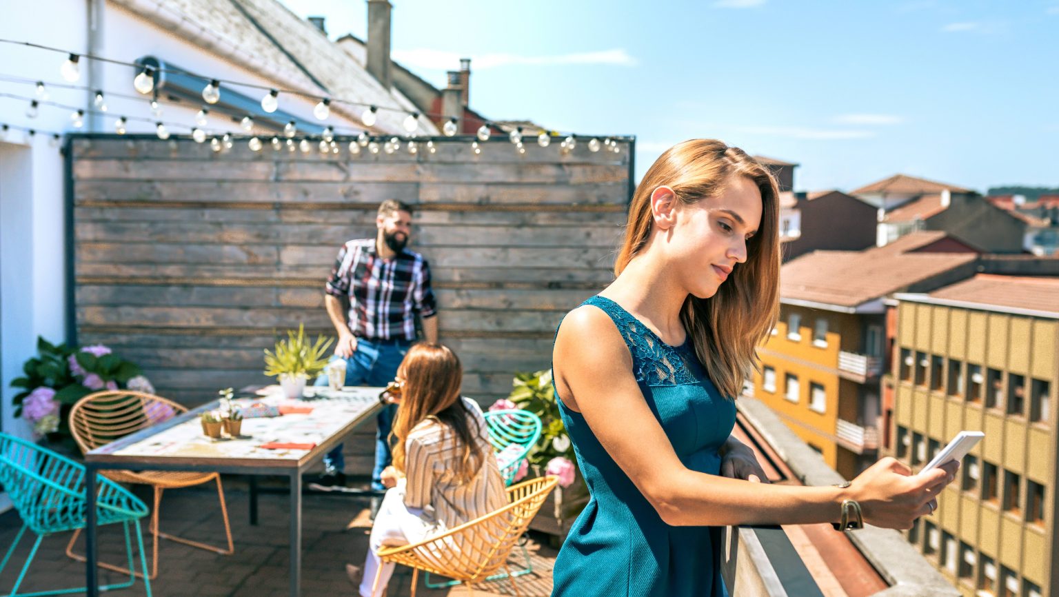 Portrait of young blonde woman with green dress looking mobile leaning on rooftop railing in a summer day